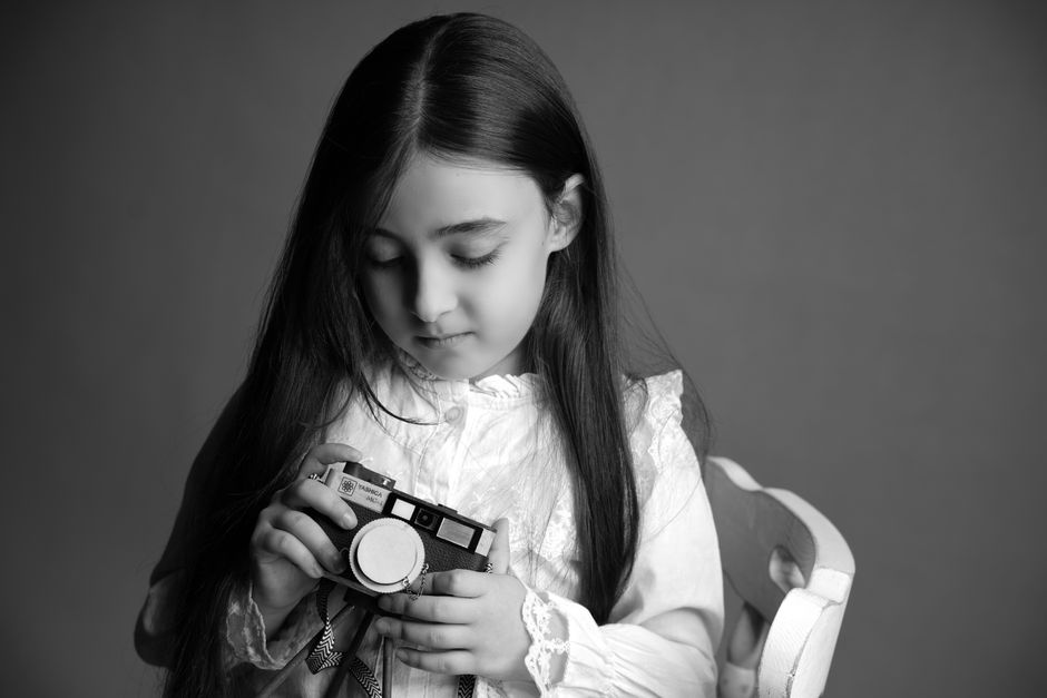 Une jeune fille tenant un appareil photo vintage dans un portrait classique en noir et blanc.