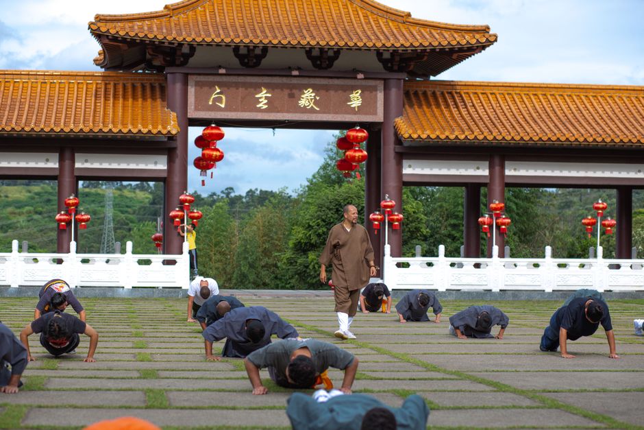 Des pratiquants d'arts martiaux s'entraînent dans la cour d'un temple à l'architecture traditionnelle.