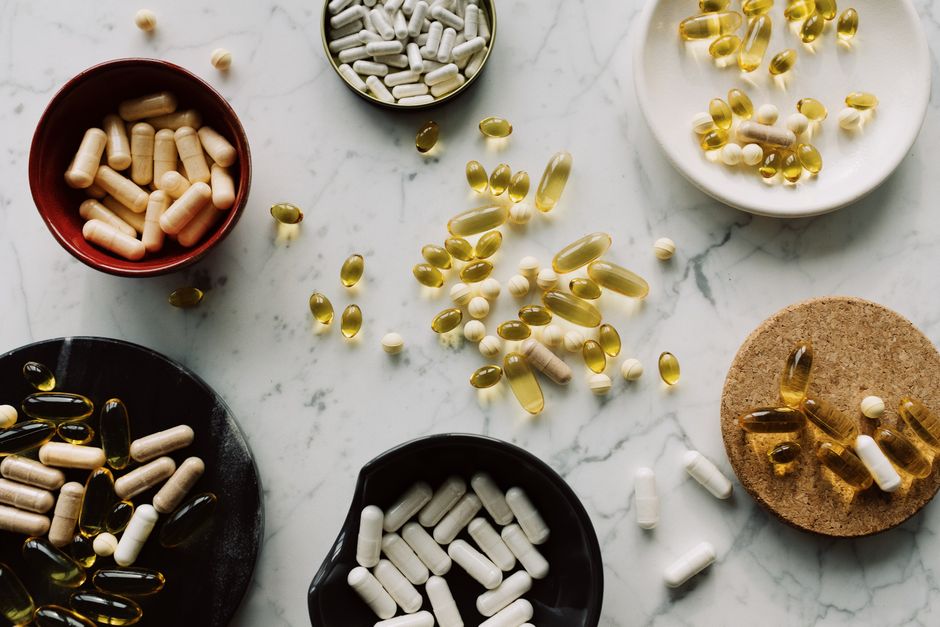 Variété de capsules et de comprimés présentés dans des bols sur une table en marbre, idéal pour des concepts de santé.
