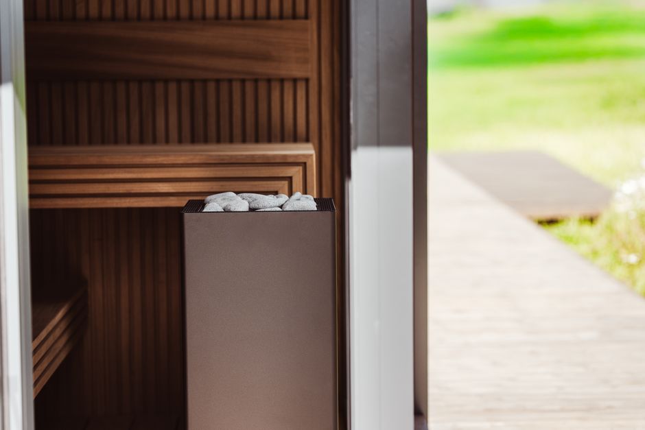 Sauna extérieur contemporain avec panneaux en bois et poêle électrique, agrémenté de pierres.