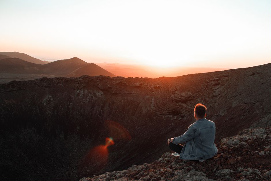 Une personne est assise au bord d'un cratère volcanique, méditant au coucher du soleil à La Oliva, Espagne.