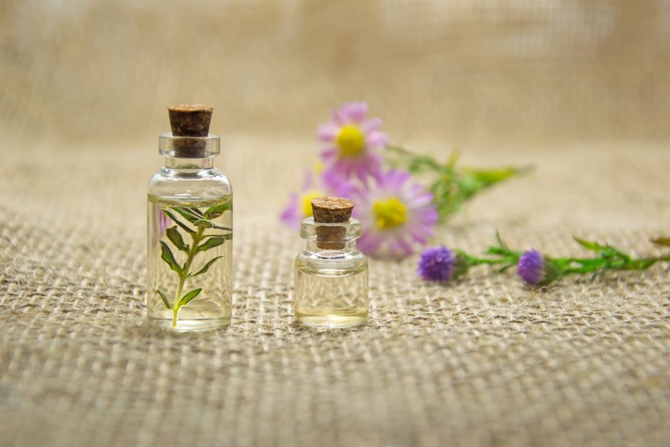 Bouteilles en verre avec des huiles essentielles et des fleurs fraîches sur un tissu en jute créant un arôme naturel.