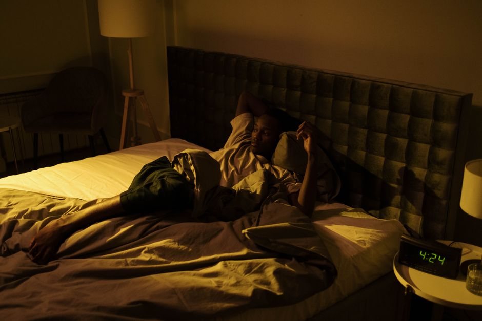 Un homme agité allongé éveillé sur son lit dans une chambre faiblement éclairée la nuit.