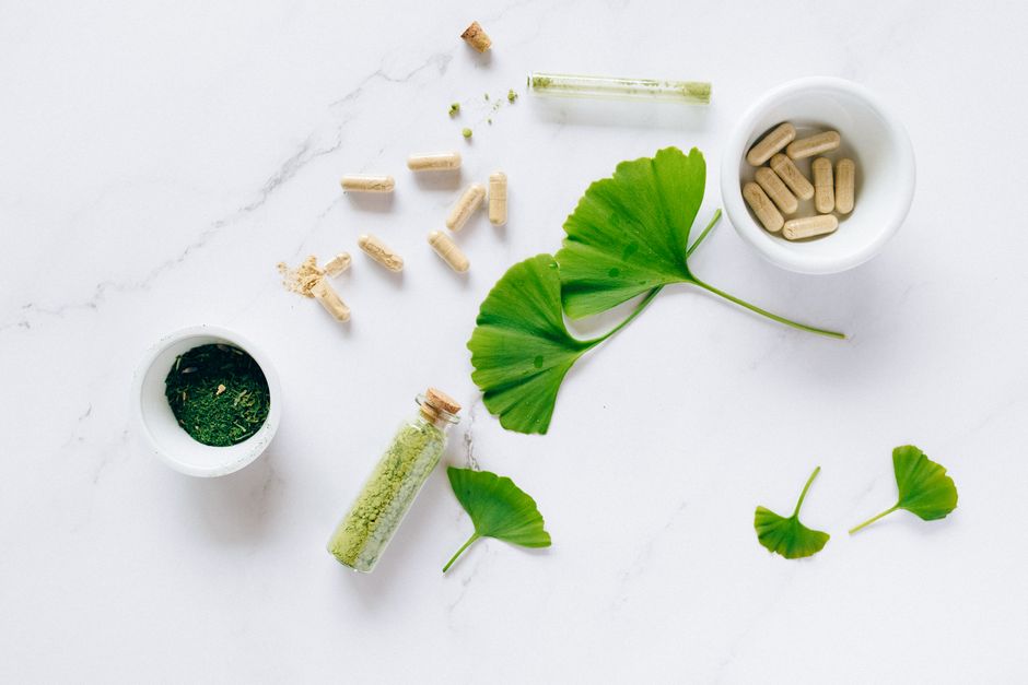 Prise de vue à plat de compléments à base de plantes avec des feuilles de ginkgo sur une surface en marbre, mettant en avant des remèdes naturels pour la santé.