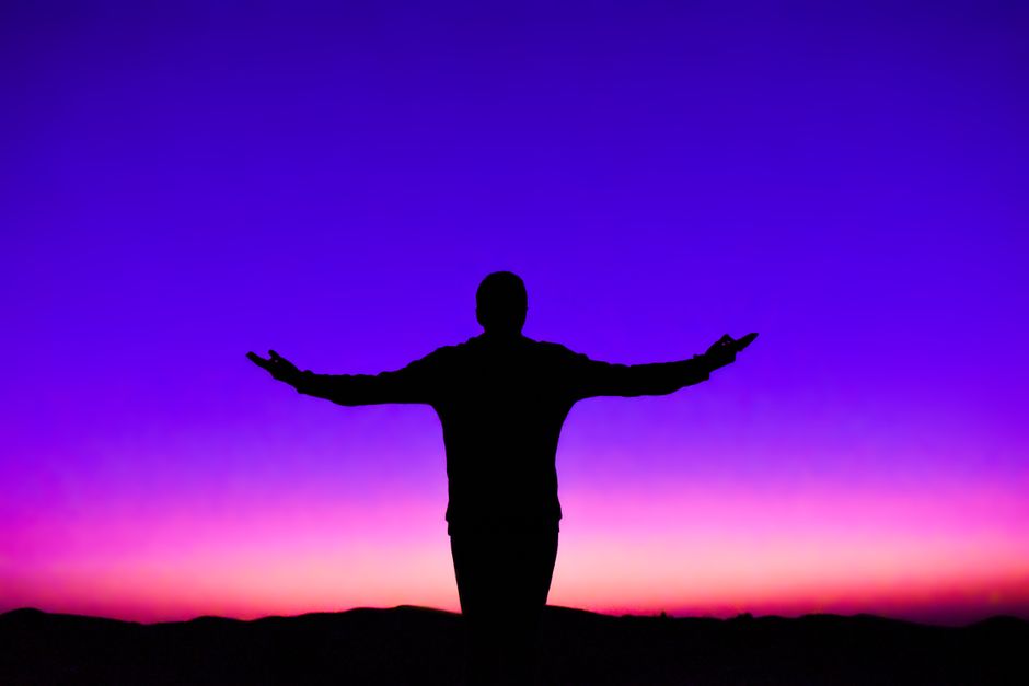 Silhouette d'une personne les bras écartés contre un ciel de coucher de soleil éclatant.