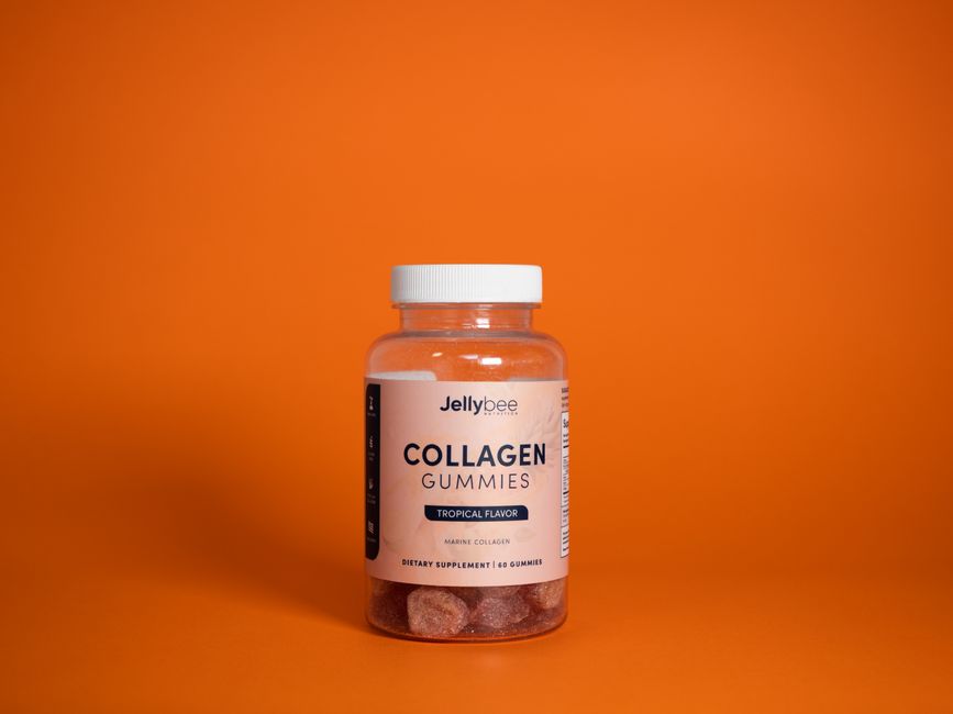 Gommes de Collagène Jellybee saveur tropicale dans une bouteille en plastique sur un fond orange.
